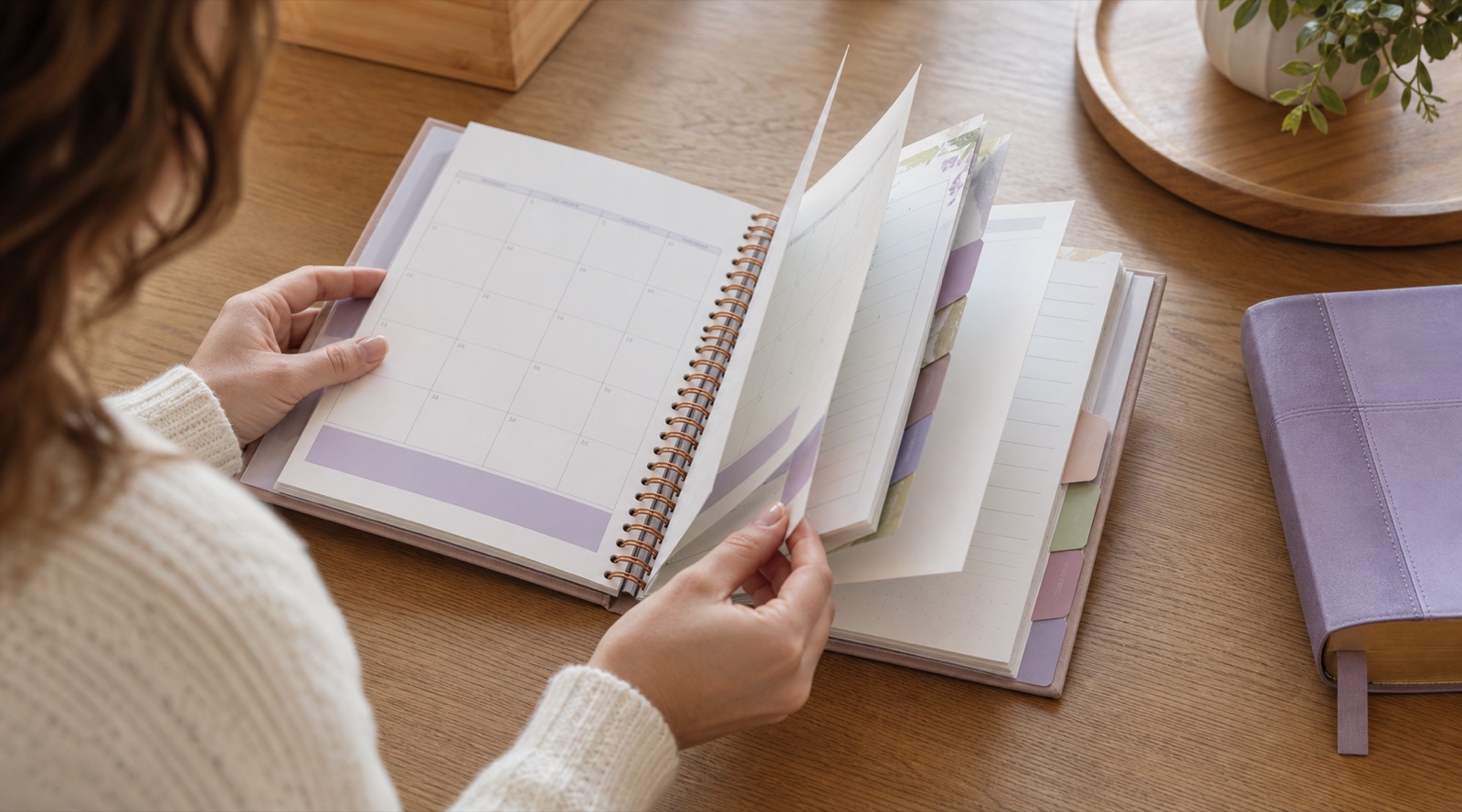 A woman turning through the blank monthly sections of a thick undated planner.